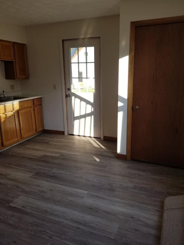 kitchen featuring dark wood finished floors, brown cabinetry, baseboards, and a sink