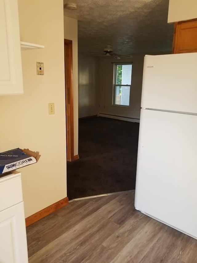 kitchen with a baseboard heating unit, wood finished floors, freestanding refrigerator, baseboards, and ceiling fan