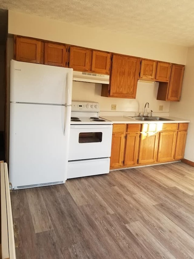 kitchen with white appliances, wood finished floors, a sink, under cabinet range hood, and a textured ceiling