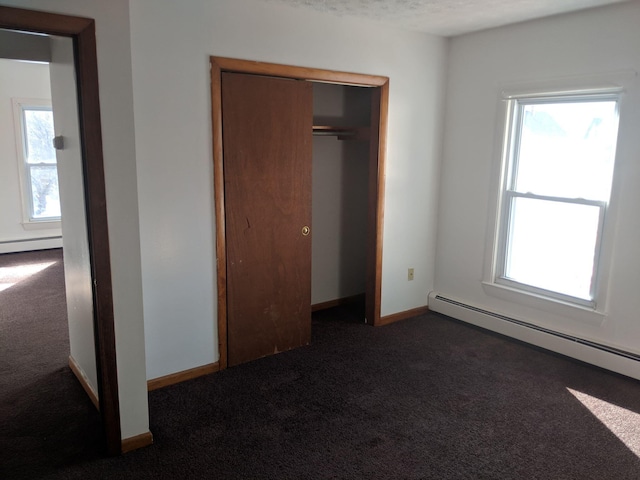 unfurnished bedroom featuring a baseboard heating unit, multiple windows, and carpet flooring