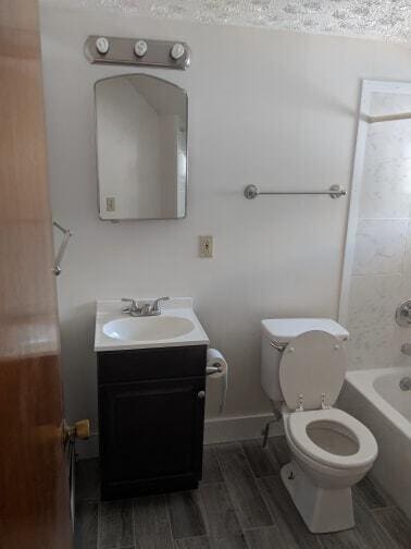 bathroom featuring wood finish floors, shower / bath combination, toilet, and vanity