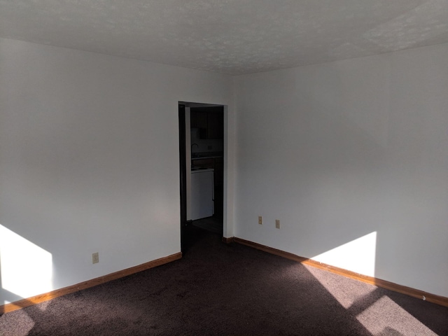 spare room with baseboards, dark colored carpet, and a textured ceiling