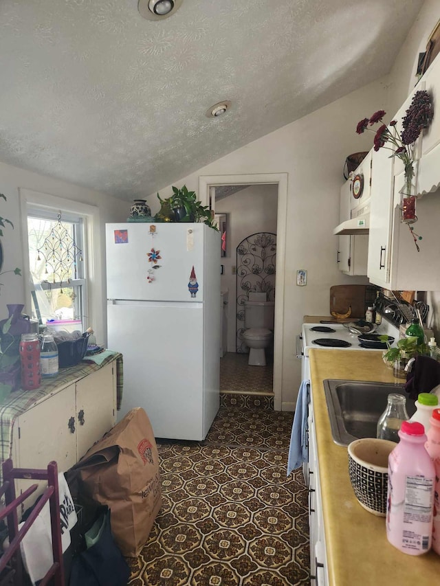 kitchen featuring lofted ceiling, open shelves, freestanding refrigerator, a textured ceiling, and white cabinetry