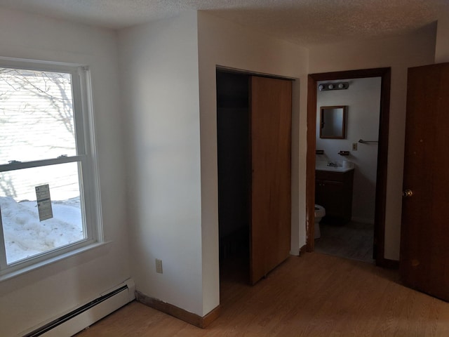 interior space with a sink, a baseboard heating unit, a textured ceiling, light wood finished floors, and baseboards