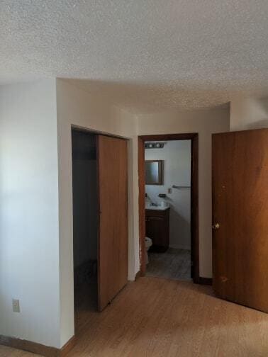 unfurnished bedroom with baseboards, a closet, a textured ceiling, light wood-type flooring, and connected bathroom