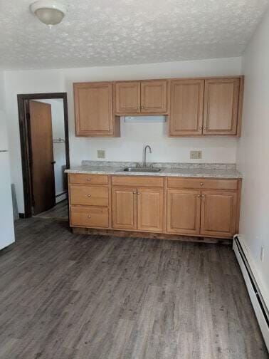 kitchen featuring dark wood-style floors, freestanding refrigerator, a sink, light countertops, and a baseboard heating unit