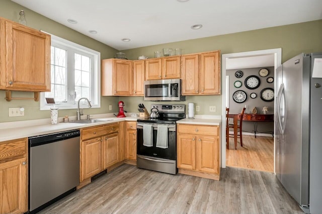 kitchen with stainless steel appliances, light wood-type flooring, light countertops, and a sink