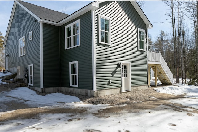 view of snow covered exterior featuring stairway and a shingled roof