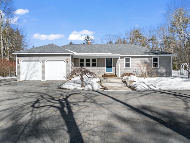 view of front facade featuring aphalt driveway, a chimney, an attached garage, and a shingled roof