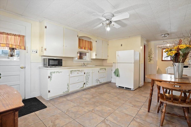 kitchen featuring light tile patterned floors, a ceiling fan, freestanding refrigerator, a sink, and light countertops