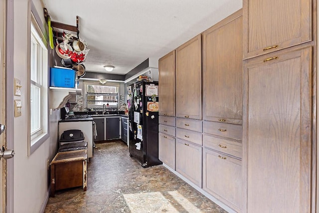 kitchen featuring stone finish flooring, range, freestanding refrigerator, and a sink