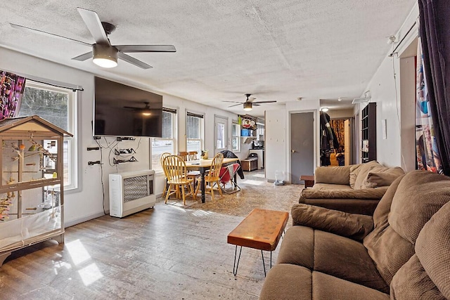 living area with heating unit, a textured ceiling, light wood-style floors, baseboards, and ceiling fan