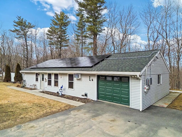 ranch-style house with solar panels, a shingled roof, a front lawn, a garage, and aphalt driveway