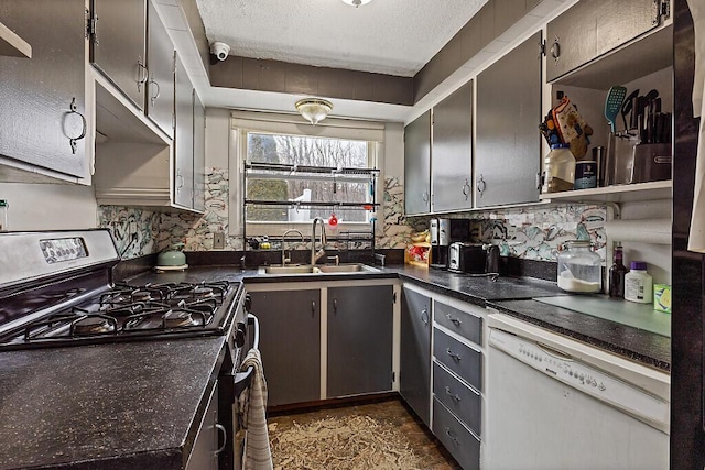 kitchen featuring stainless steel gas range oven, dark countertops, white dishwasher, and a sink