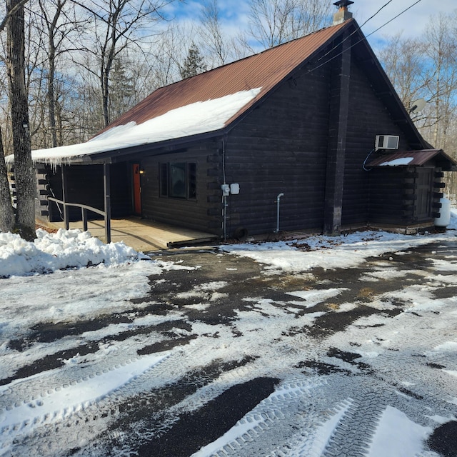 view of snow covered exterior with a carport, an AC wall unit, and a chimney