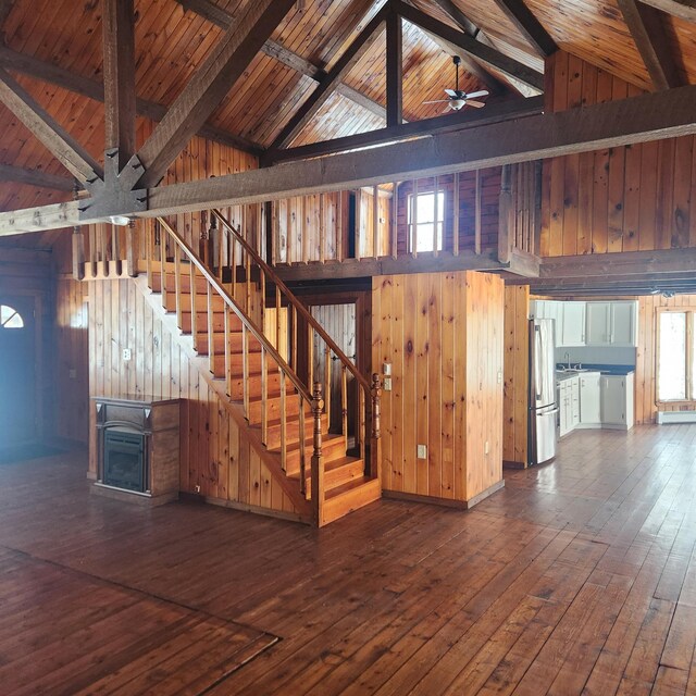 staircase featuring hardwood / wood-style floors, beam ceiling, wooden walls, and ceiling fan