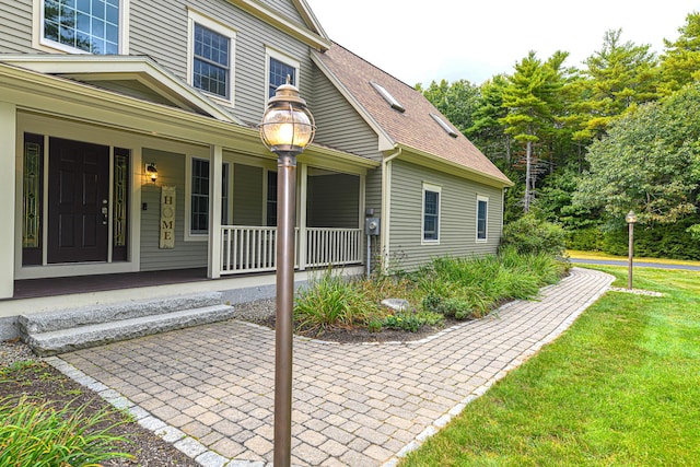 entrance to property with a porch, a yard, and a shingled roof