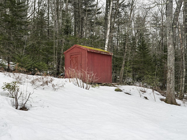 snow covered structure with a forest view, an outbuilding, and a storage shed