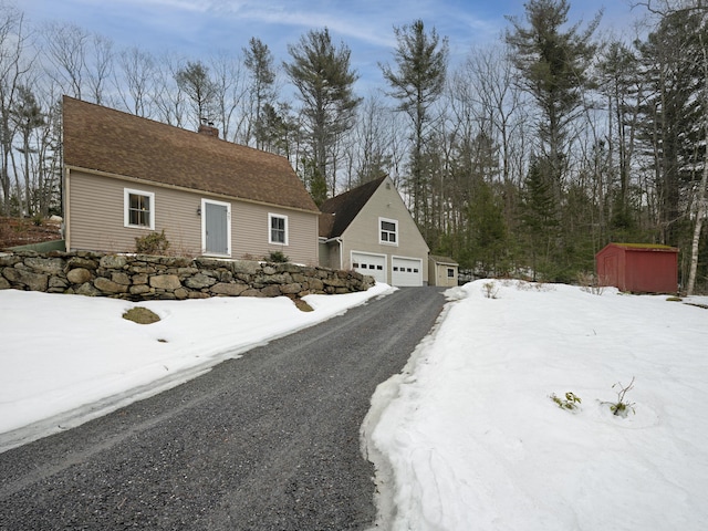 view of front facade with an outbuilding, a chimney, aphalt driveway, and a garage