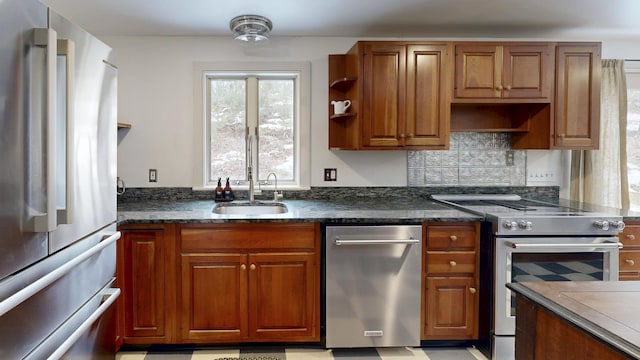 kitchen featuring dark stone counters, decorative backsplash, brown cabinets, stainless steel appliances, and a sink