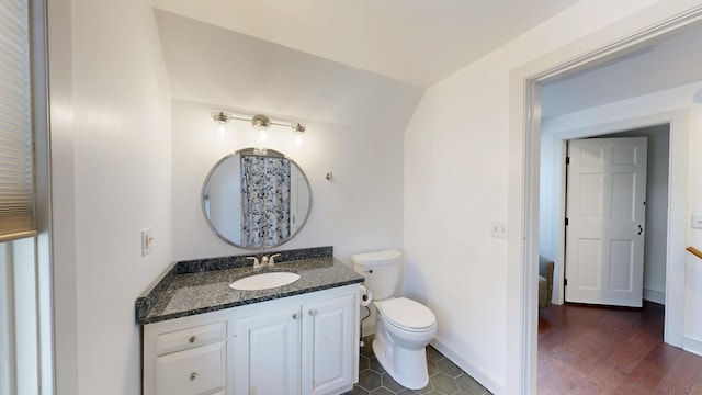 bathroom featuring baseboards, toilet, vanity, and vaulted ceiling