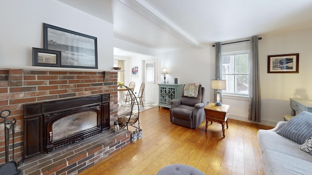 living area featuring beamed ceiling, a fireplace, light wood-type flooring, and baseboards