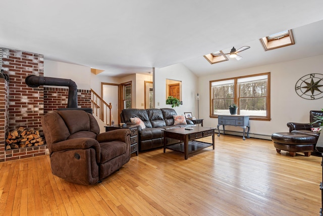 living area featuring a baseboard heating unit, a skylight, a wood stove, and light wood finished floors