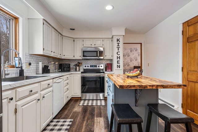 kitchen with a sink, tasteful backsplash, dark wood finished floors, appliances with stainless steel finishes, and butcher block counters