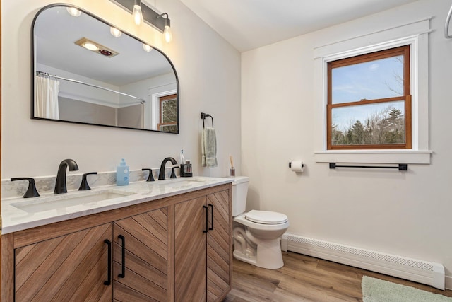 full bathroom with a sink, a baseboard radiator, toilet, and wood finished floors