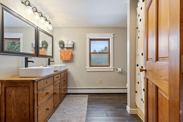 bathroom featuring a sink, baseboard heating, wood finished floors, and double vanity