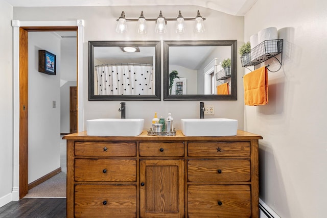 full bath with a sink, a baseboard radiator, baseboards, and double vanity