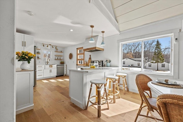 kitchen with stainless steel dishwasher, a peninsula, white cabinets, and a breakfast bar