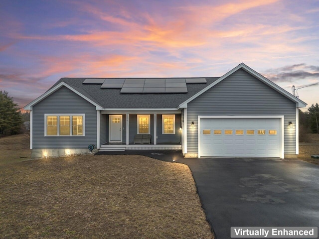ranch-style home featuring aphalt driveway, a porch, an attached garage, a shingled roof, and solar panels