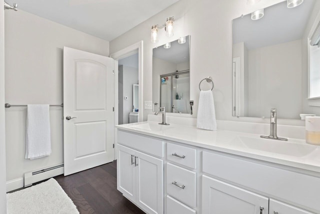 bathroom featuring a baseboard heating unit, double vanity, a stall shower, and a sink