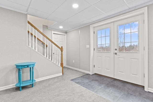 foyer with a drop ceiling, carpet floors, baseboards, and stairs