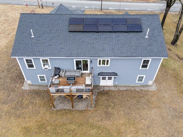 back of house featuring roof mounted solar panels, a wooden deck, and a shingled roof