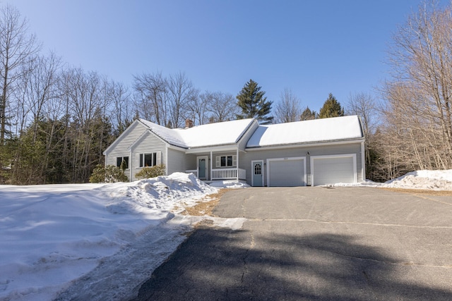 ranch-style house featuring aphalt driveway, an attached garage, a porch, and a chimney