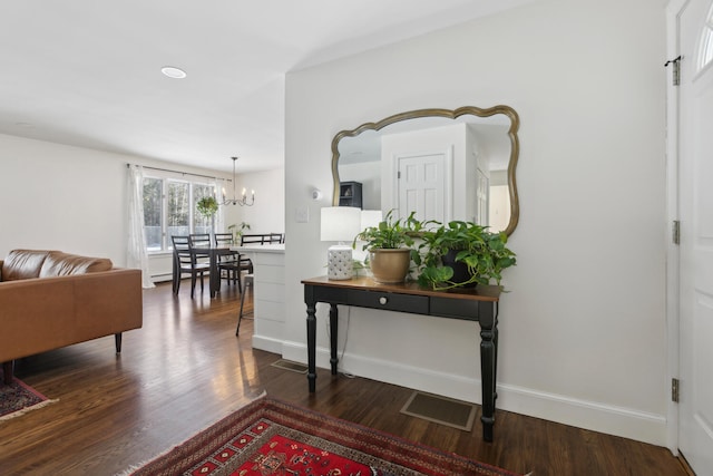 corridor featuring an inviting chandelier, wood finished floors, visible vents, and baseboards