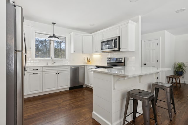 kitchen with a sink, backsplash, dark wood-style floors, appliances with stainless steel finishes, and a peninsula