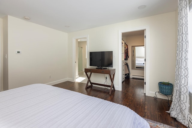 bedroom with a spacious closet, a baseboard heating unit, baseboards, and dark wood-style flooring