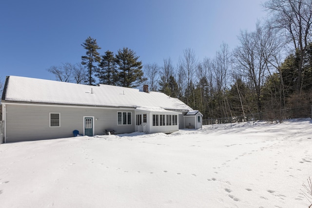 snow covered rear of property featuring a chimney and a sunroom