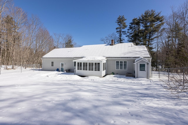 snow covered house featuring fence, a sunroom, and a chimney