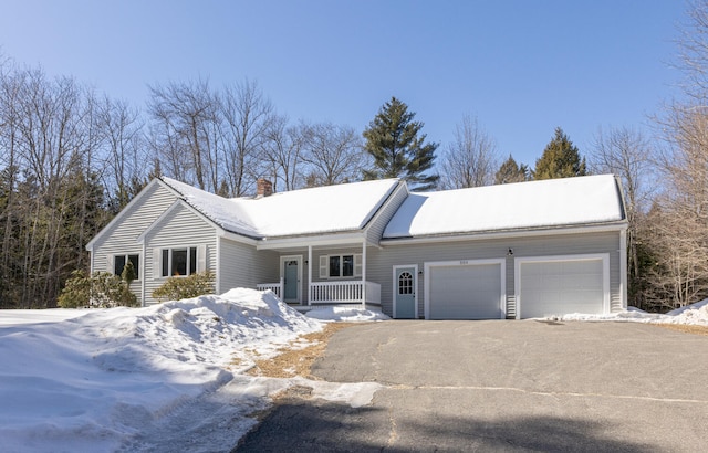 ranch-style home with a garage, covered porch, a chimney, and aphalt driveway