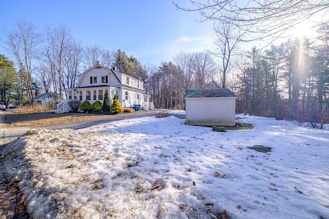 snow covered property featuring a gambrel roof, a storage shed, and an outdoor structure