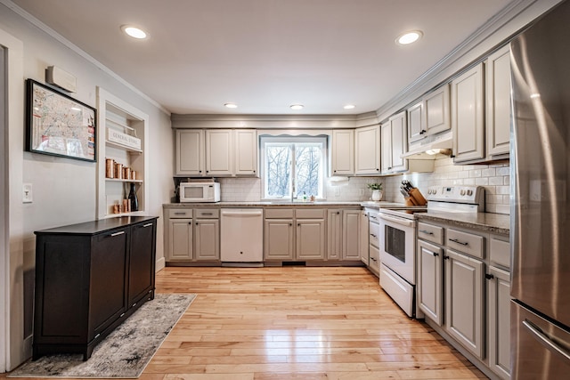 kitchen with white appliances, a sink, under cabinet range hood, crown molding, and light wood-type flooring