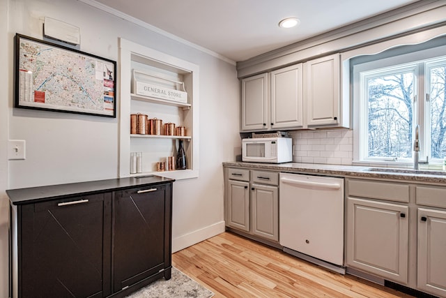 kitchen with white appliances, light wood finished floors, ornamental molding, decorative backsplash, and a sink