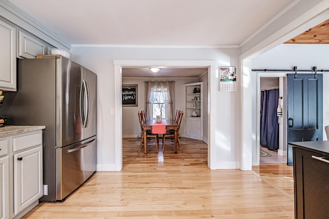 kitchen with light wood-style flooring, freestanding refrigerator, ornamental molding, light countertops, and a barn door