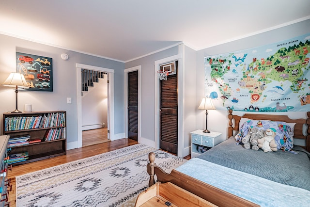 bedroom with crown molding, a baseboard heating unit, baseboards, and wood finished floors