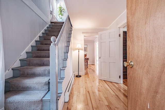 staircase featuring hardwood / wood-style floors, baseboards, baseboard heating, and ornamental molding