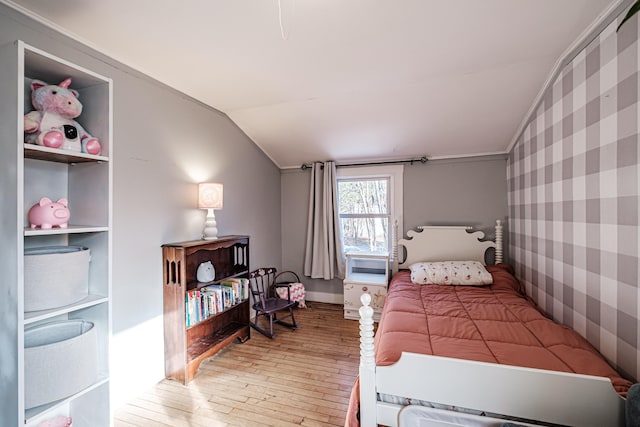 bedroom featuring wallpapered walls, light wood-type flooring, lofted ceiling, and an accent wall